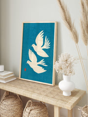 Two white flying doves minimalist art print on a vibrant blue background with a red artist's, in an alternate framed mockup