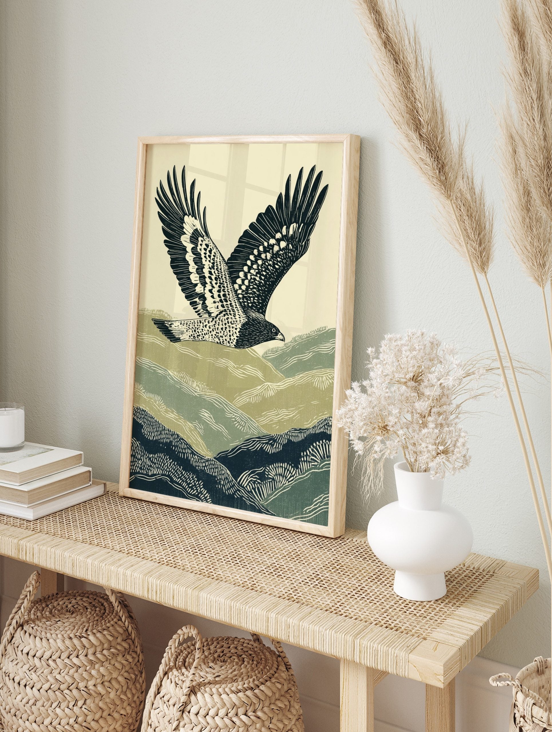 Illustrative print of a hawk flying over green and navy rolling hills against a pale sky, in an alternate framed mockup