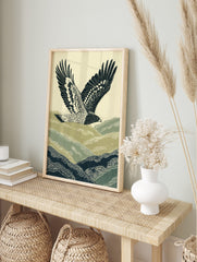 Illustrative print of a hawk flying over green and navy rolling hills against a pale sky, in an alternate framed mockup