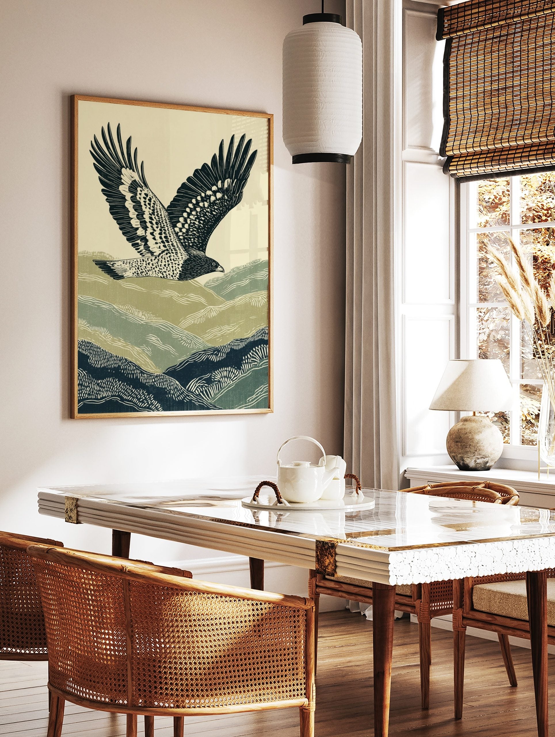 Illustrative print of a hawk flying over green and navy rolling hills against a pale sky, in a styled room mockup