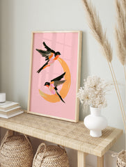 Painterly illustration of two swallows flying around an orange crescent moon on a pink, in an alternate framed mockup