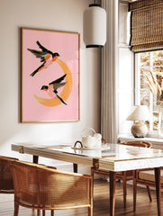 Painterly illustration of two swallows flying around an orange crescent moon on a pink background, in a styled room mockup