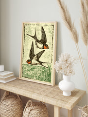 Illustrative print of two black and orange swallows flying over green water, with a woodcut, in an alternate framed mockup