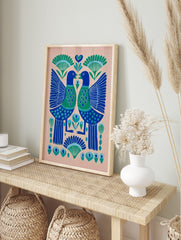 Symmetrical folk art print of two blue and green birds with heart chests and botanical motifs, in an alternate framed mockup