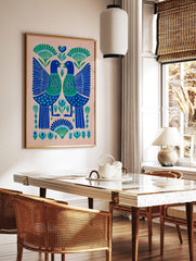 Symmetrical folk art print of two blue and green birds with heart chests and botanical motifs on a, in a styled room mockup