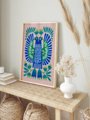 Stylised folk art print of two blue birds with green wings and white patterns, on a pink, in an alternate framed mockup