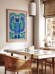 Stylised folk art print of two blue birds with green wings and white patterns, on a pink background, in a styled room mockup