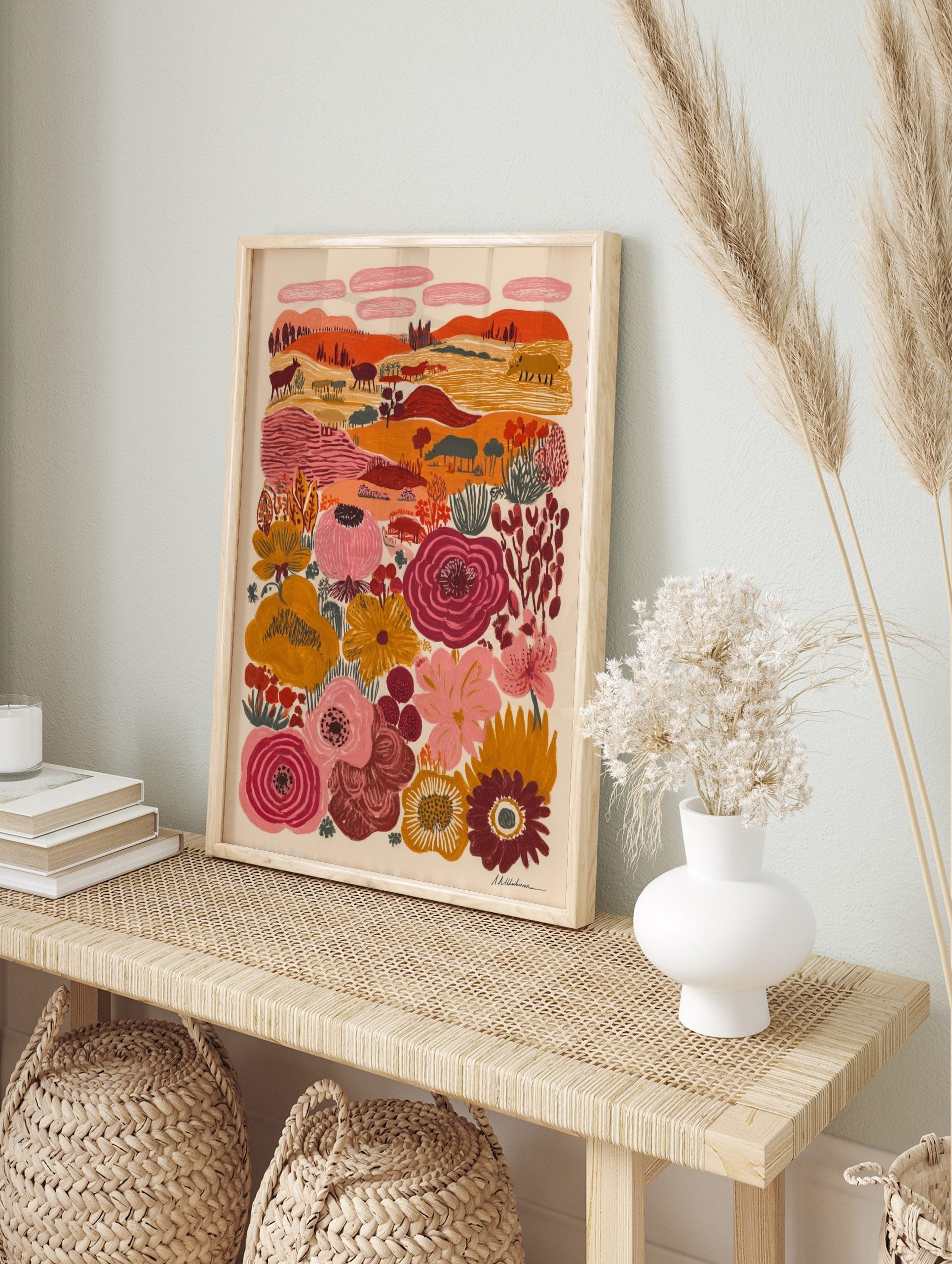 Folk art landscape print with stylized animals, trees, hills, and large colourful flowers in, in an alternate framed mockup