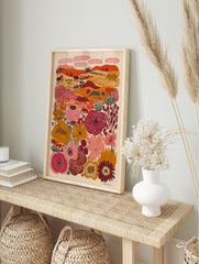 Folk art landscape print with stylized animals, trees, hills, and large colourful flowers in, in an alternate framed mockup