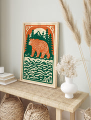 Illustrative forest bear print with orange bear, green pine trees, mountains, and cream water, in an alternate framed mockup