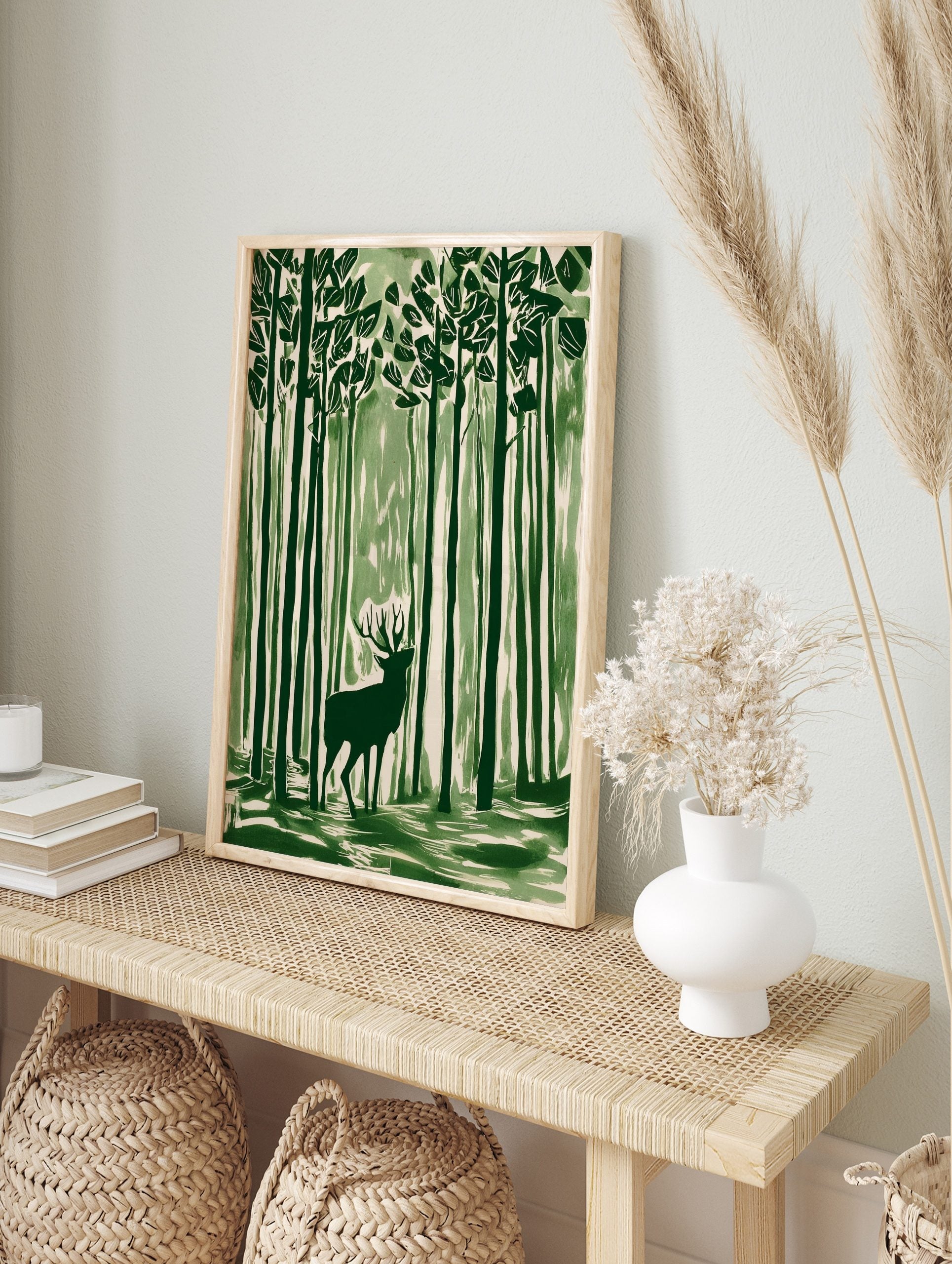 Green illustrative wall art print of a stag with antlers standing in a tall forest, looking, in an alternate framed mockup