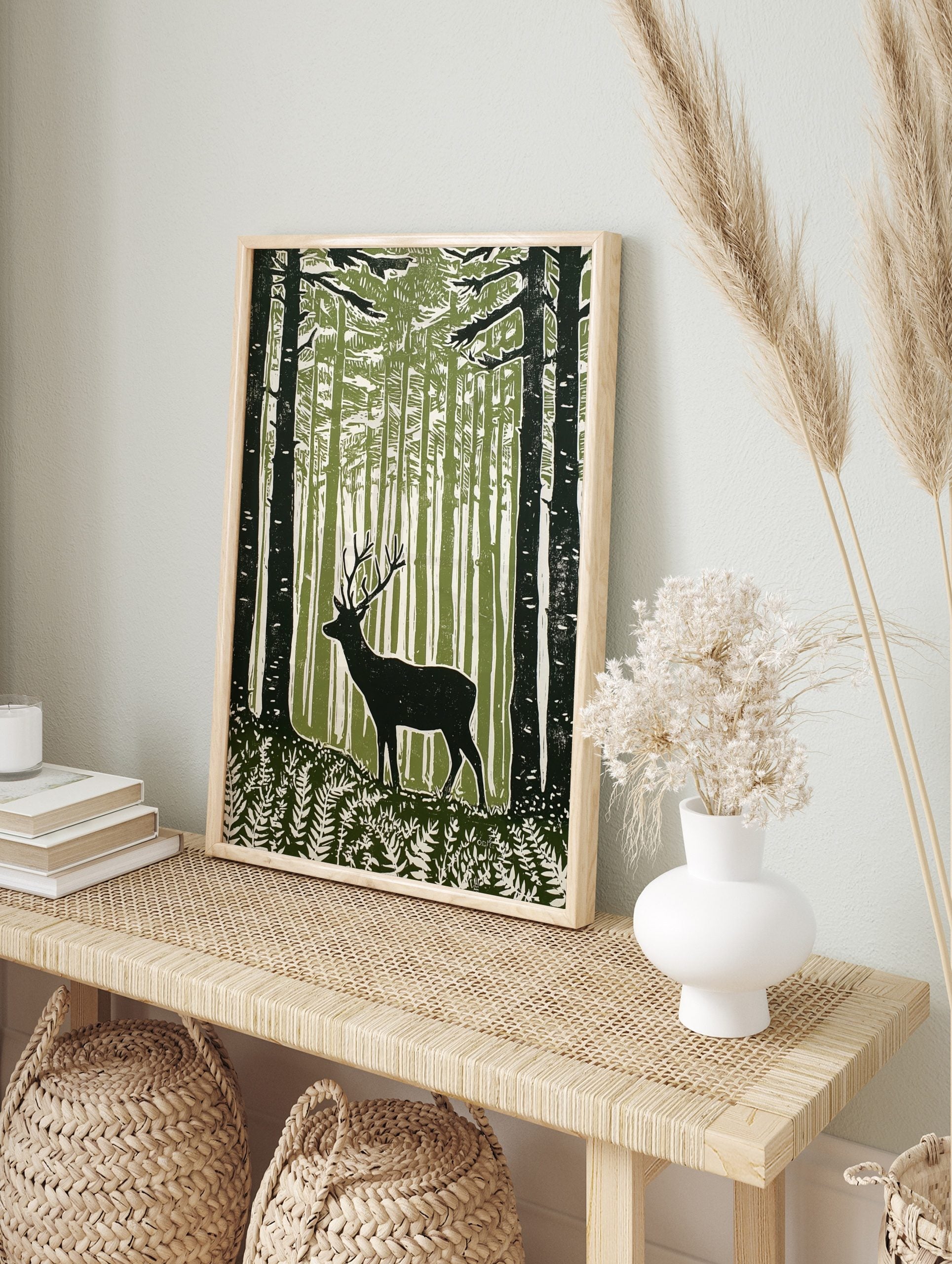 Green woodcut print of a stag with antlers in a dense forest with ferns and tall trees, in an alternate framed mockup