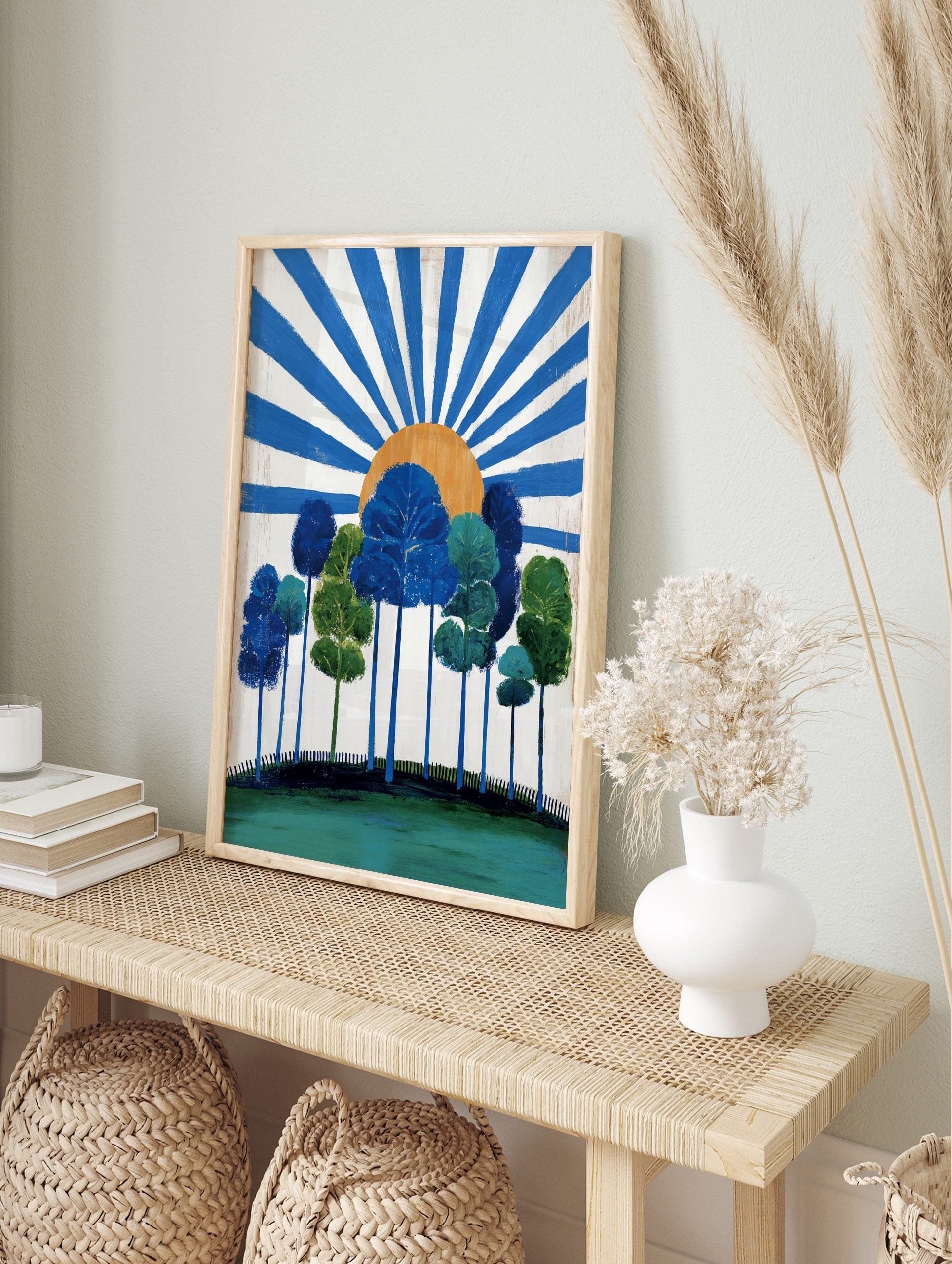 Stylised blue and green trees on a hill with an orange sun and radiating blue rays on a white, in an alternate framed mockup