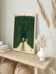 Illustrative art print of a red train travelling through a dense green forest with a small, in an alternate framed mockup