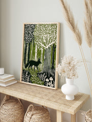 Linocut style print of a dark green fox walking through a cream and green forest with trees, in an alternate framed mockup