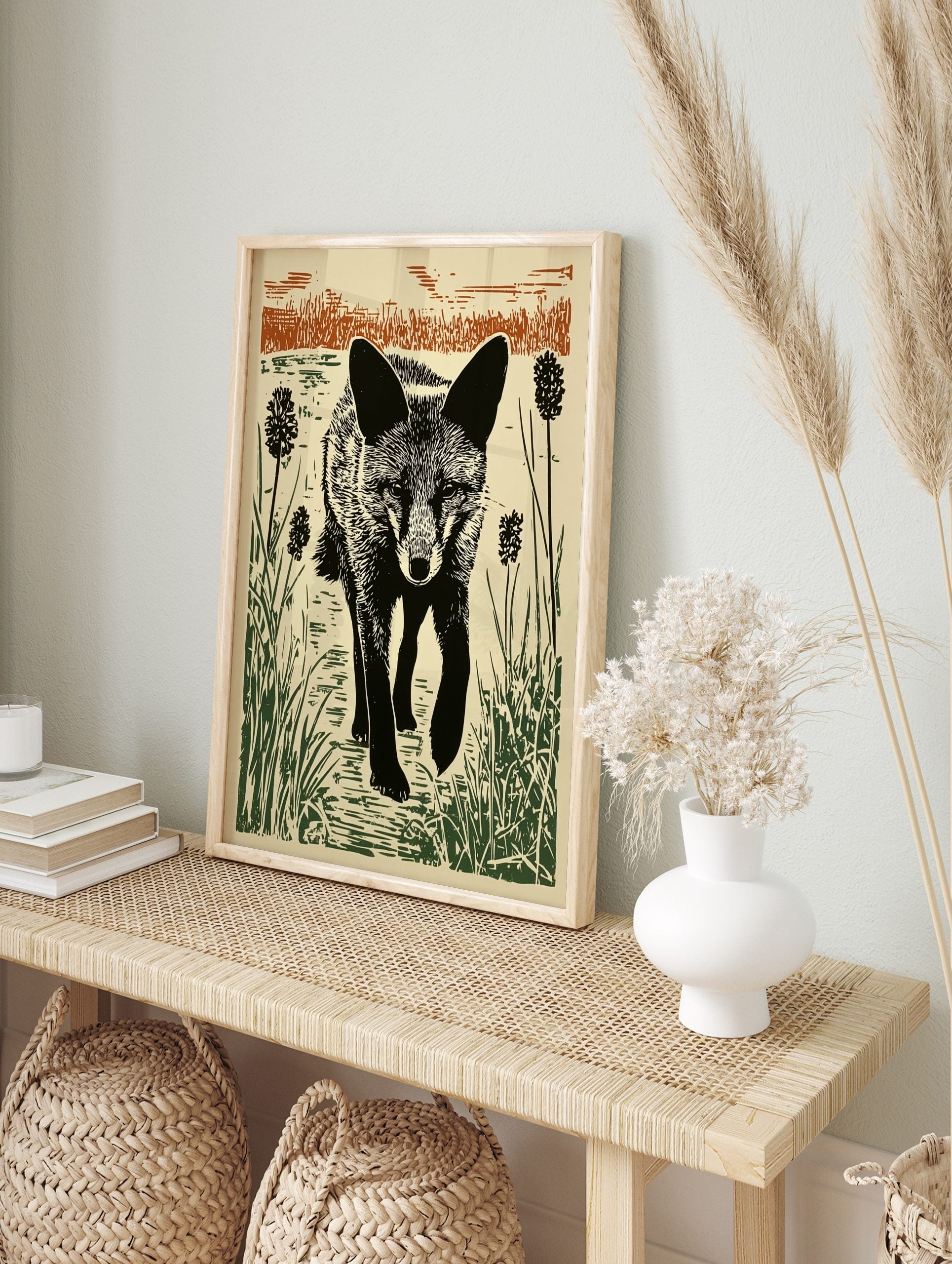 Linocut style print of a black fox walking through green reeds and brown grasses against a, in an alternate framed mockup