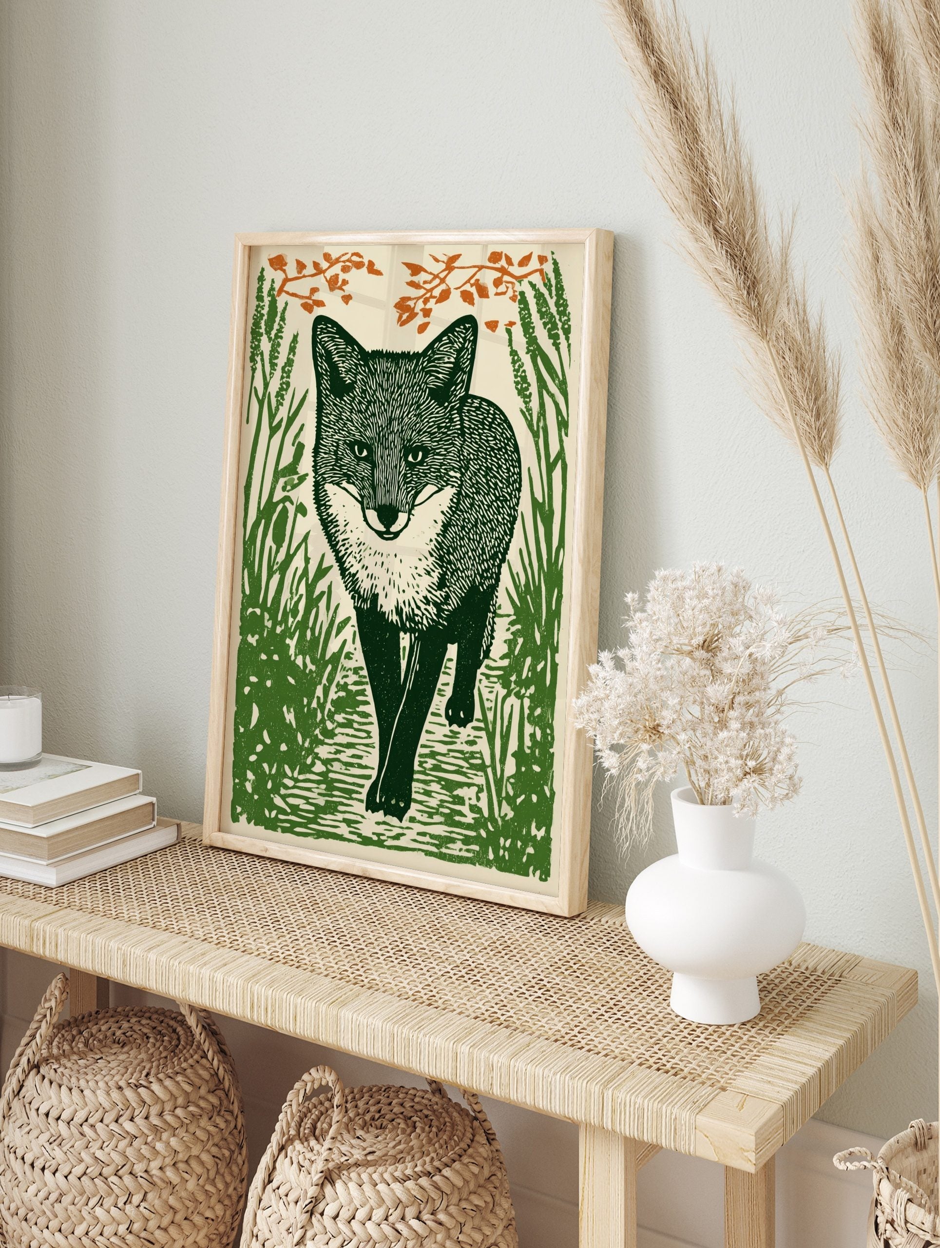Linocut style art print of a fox walking through tall green grass with orange foliage above, in an alternate framed mockup