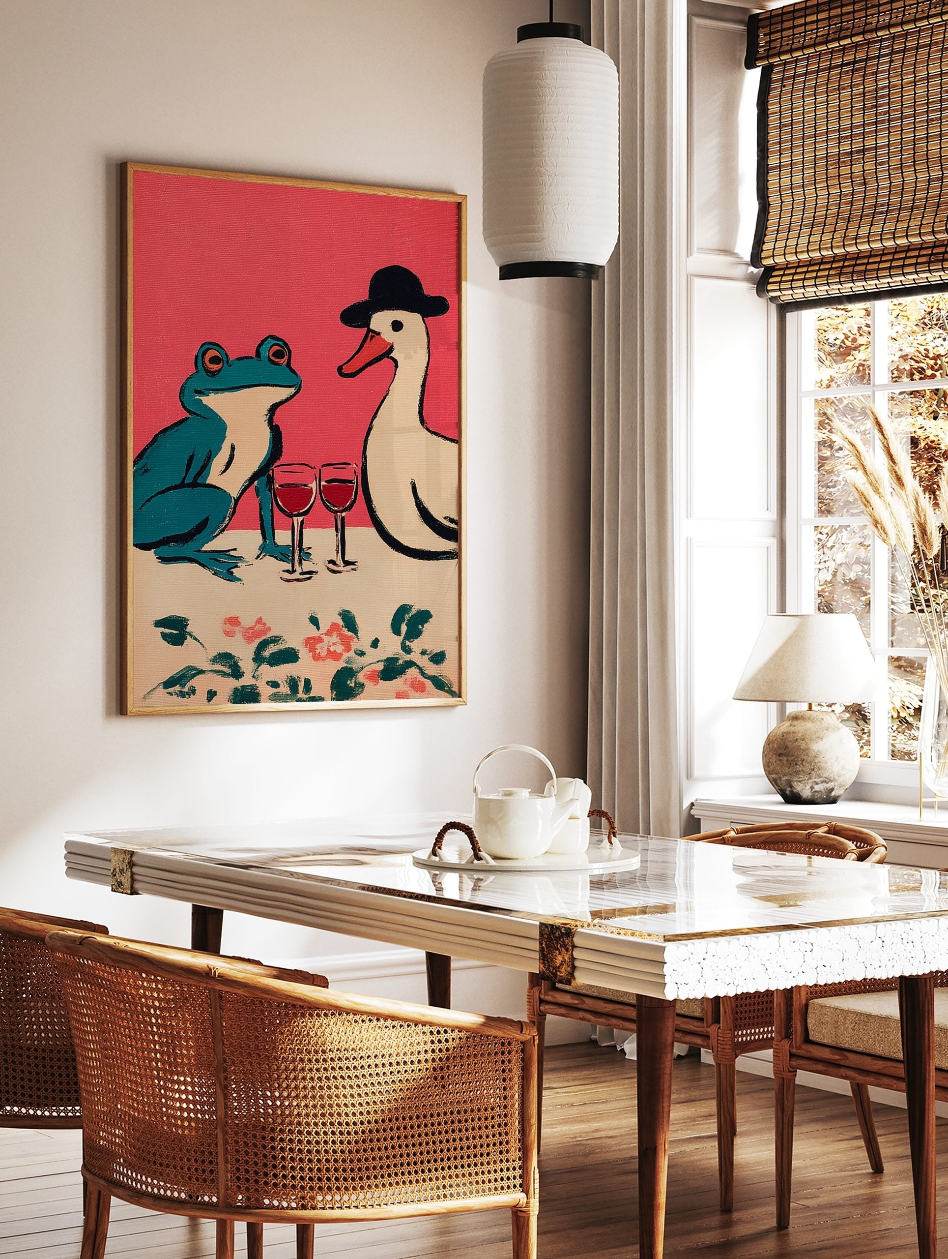 Illustrative print of a teal frog and a white duck in a hat sharing red wine on a pink background, in a styled room mockup