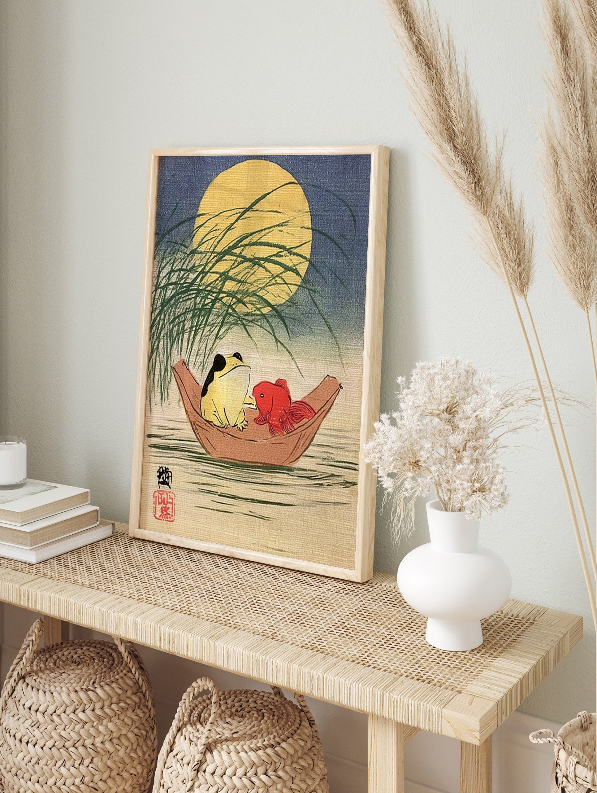 Japanese-style illustration of a frog and a red goldfish in a wooden boat under a full moon, in an alternate framed mockup