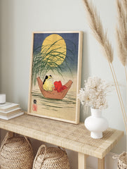 Japanese-style illustration of a frog and a red goldfish in a wooden boat under a full moon, in an alternate framed mockup