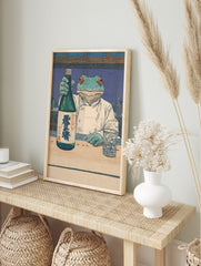 Frog chef in white coat holding sake bottle with kanji text, woodblock style print at a bar, in an alternate framed mockup