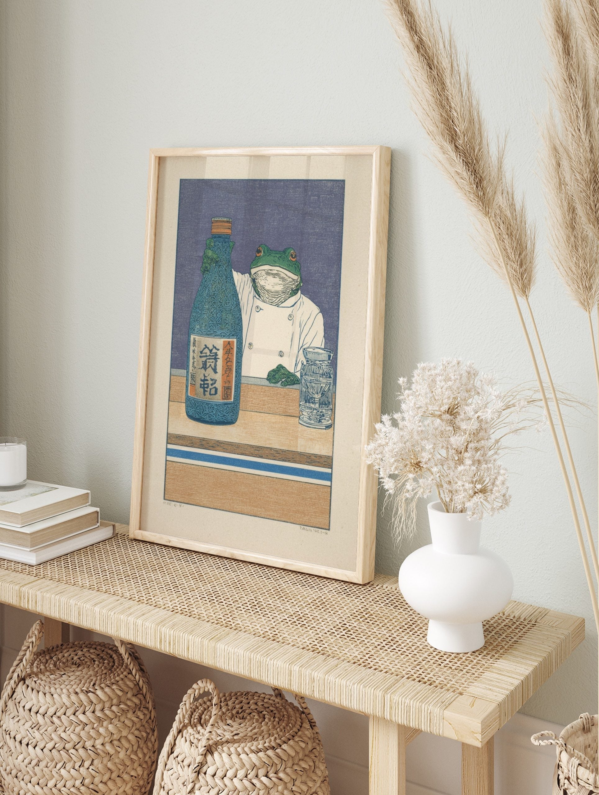 Illustrative print of a frog chef holding a blue sake bottle with Japanese Kanji on a wooden, in an alternate framed mockup