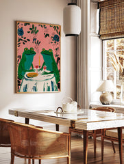 Two whimsical green frogs on a date at a table with wine and candle, pink background with leaves, in a styled room mockup