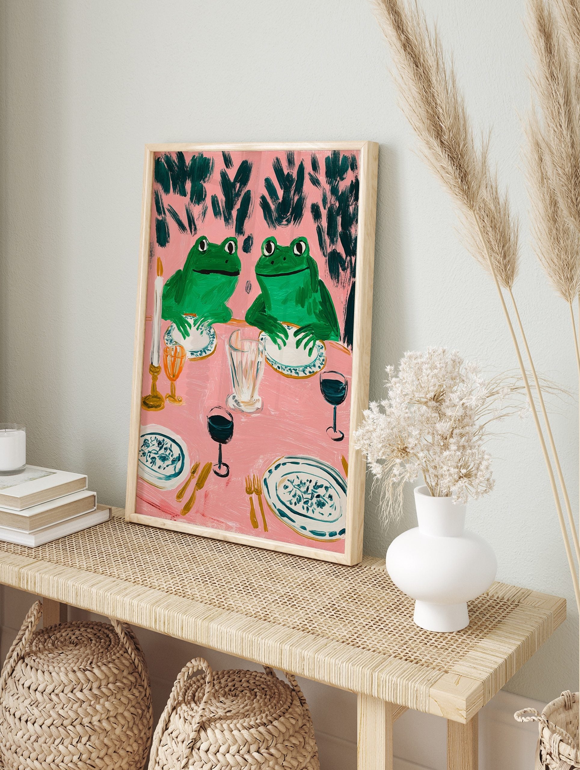 Humorous frog dinner party art print with two green frogs at a pink table set with plates, in an alternate framed mockup