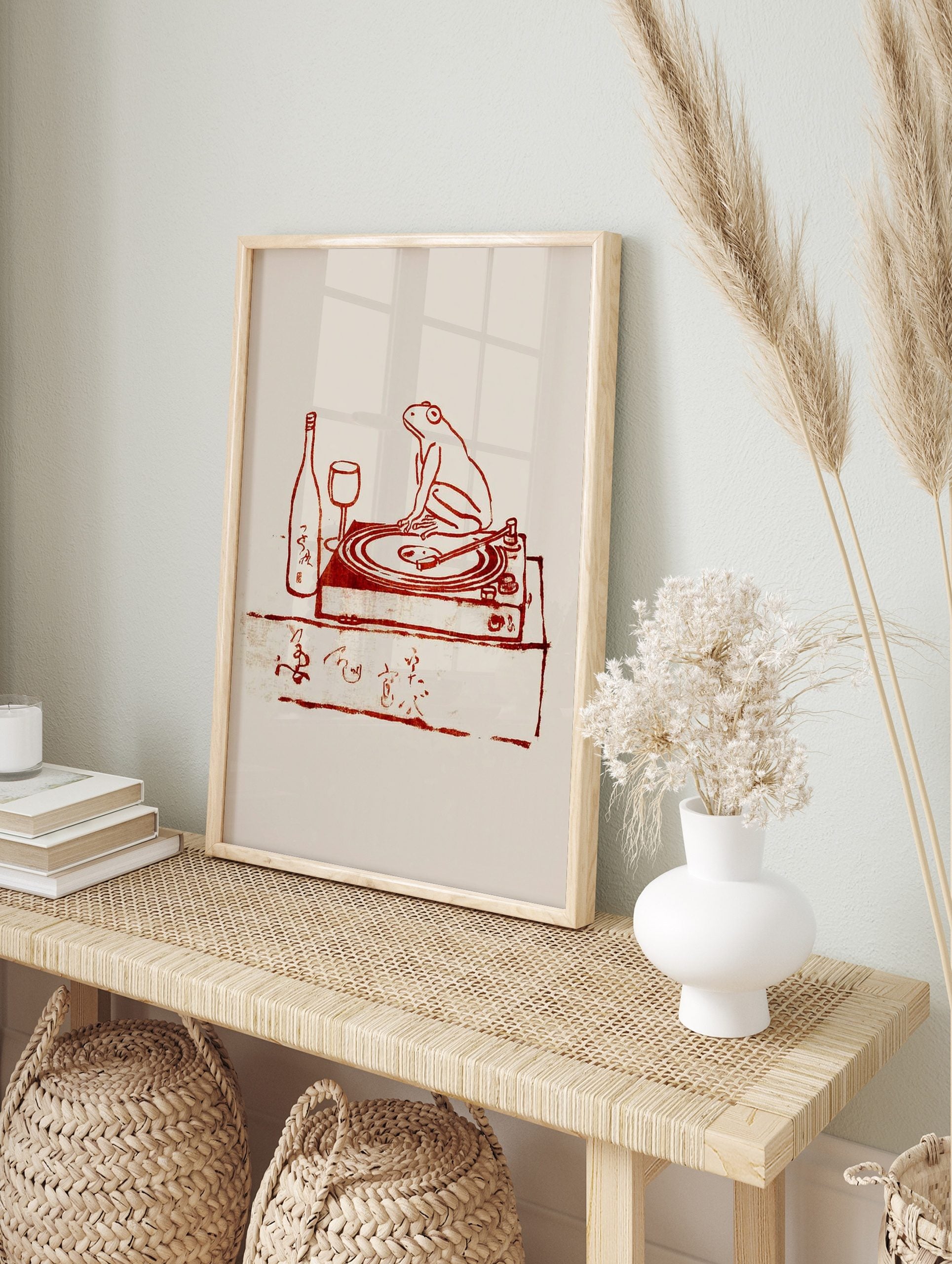 Reddish-brown illustration of a frog on a turntable with a wine bottle, glass, and Japanese, in an alternate framed mockup