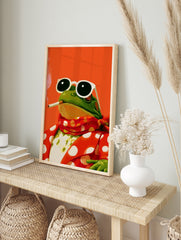 Illustration of a frog wearing sunglasses and a red polka-dot suit, smoking, against a bright, in an alternate framed mockup