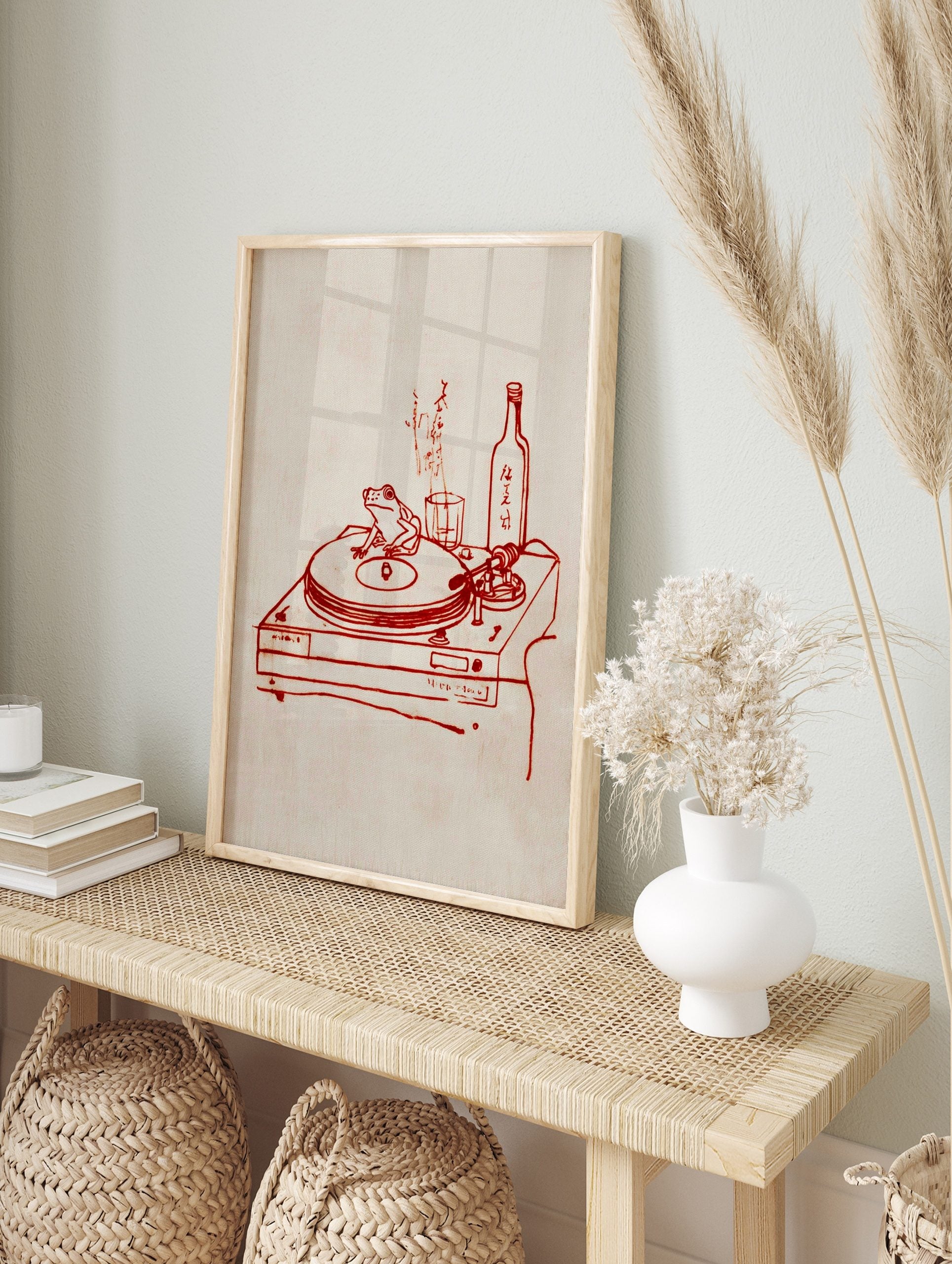 Red line art of a frog on a turntable, with a sake bottle, glass, and Japanese text on a, in an alternate framed mockup