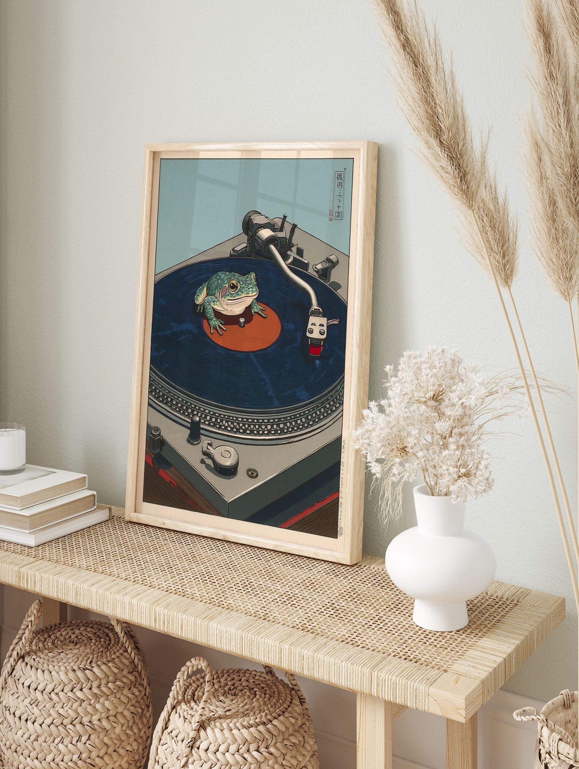 Japanese style illustration of a green frog sitting on a dark blue vinyl record on a grey, in an alternate framed mockup
