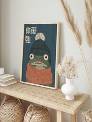 Illustrative frog wall art wearing a blue beanie and orange scarf with Japanese text on a dark blue background, cozy animal print. - Image 3
