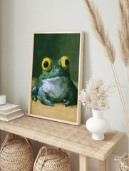 Painterly frog wall art with large yellow eyes and green textured skin against a dark, in an alternate framed mockup