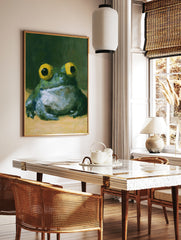 Painterly frog wall art with large yellow eyes and green textured skin against a dark background, in a styled room mockup
