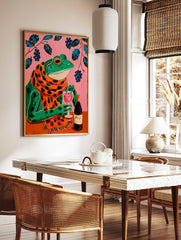 Illustrative wall art of a green frog in a polka-dot scarf, holding a wine glass on a pink, in a styled room mockup