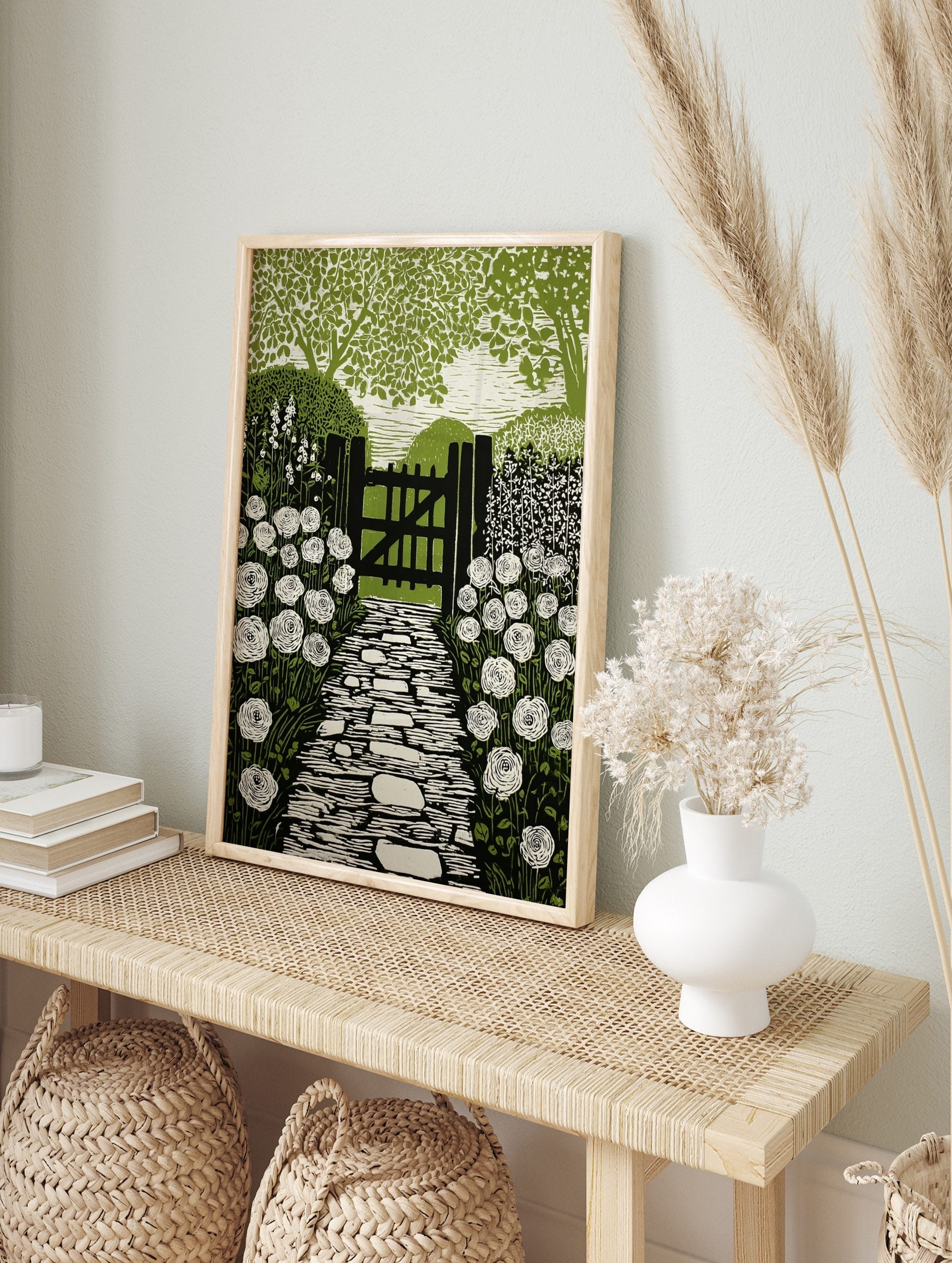Linocut style print of a garden path leading to a wooden gate, flanked by white roses and, in an alternate framed mockup