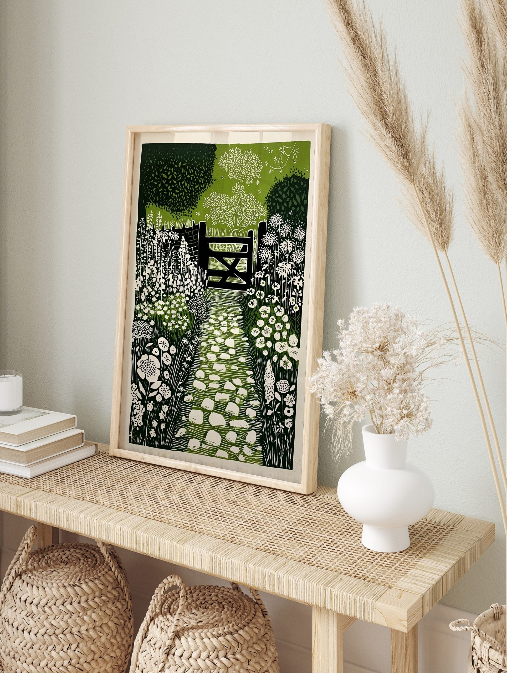 Linocut style garden path leading to a gate with white flowers and green foliage wall art, in an alternate framed mockup
