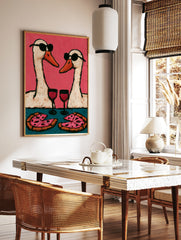 Playful wall art print of two geese wearing sunglasses, drinking wine, and eating pizza against a, in a styled room mockup