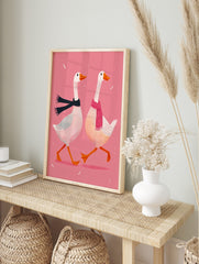 Two white geese in black and pink scarves walking on a pink background with white feathers, in an alternate framed mockup