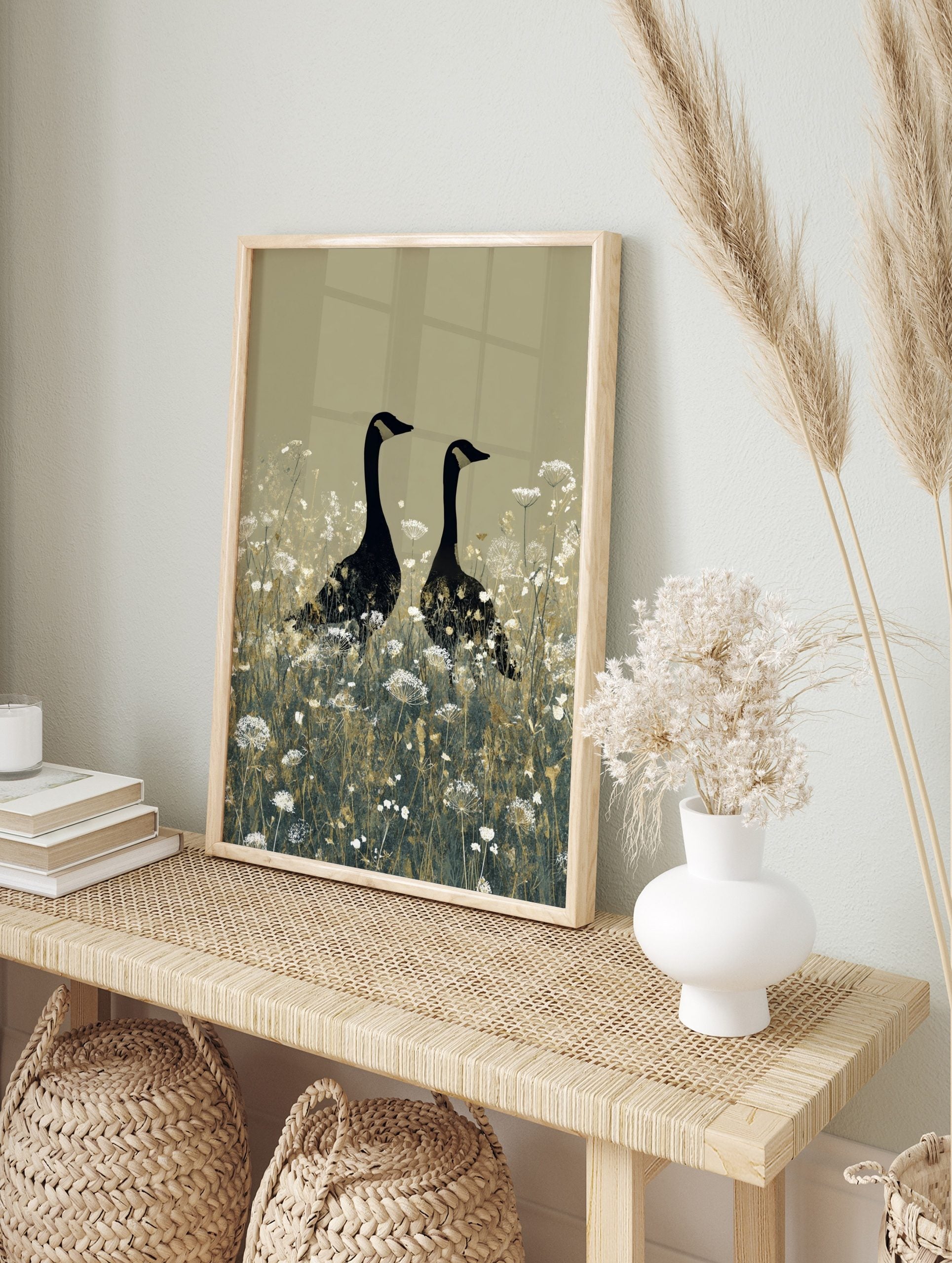 Two black geese with gold head markings standing in a field of white wildflowers on a beige, in an alternate framed mockup
