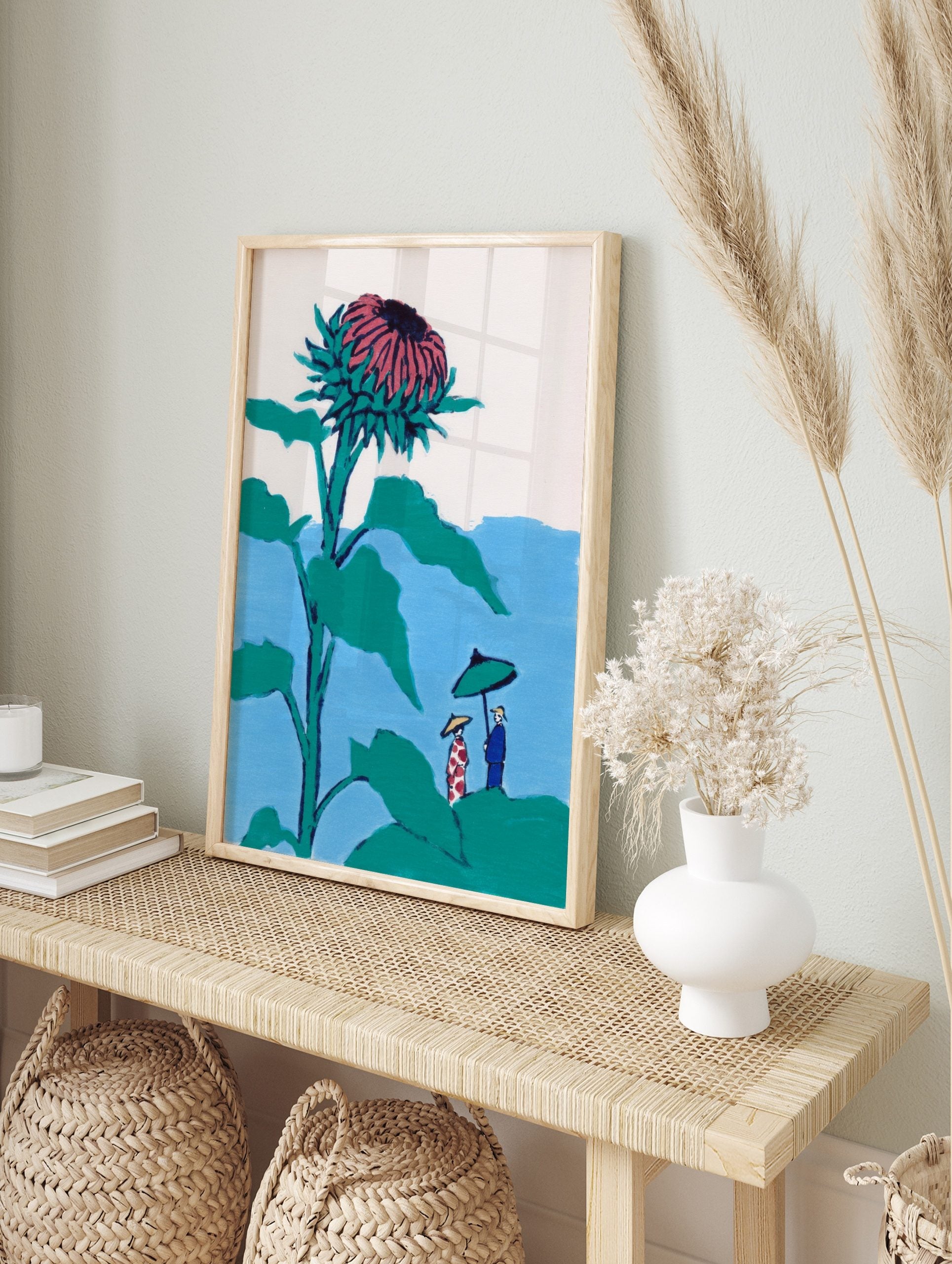Illustrative print of a giant teal and pink thistle flower towering over two small figures, in an alternate framed mockup
