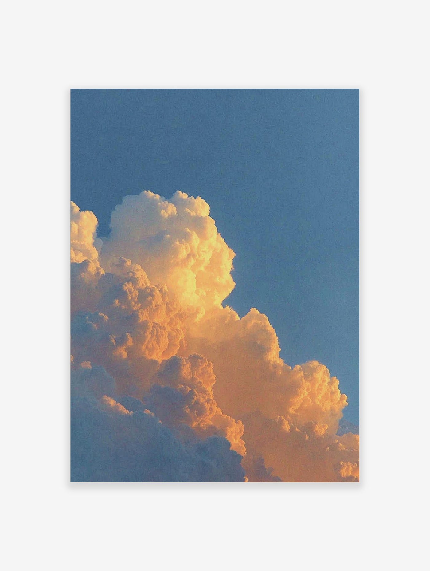 Close-up of cumulus clouds bathed in warm orange and yellow light against a blue sky