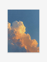 Close-up of cumulus clouds bathed in warm orange and yellow light against a blue sky