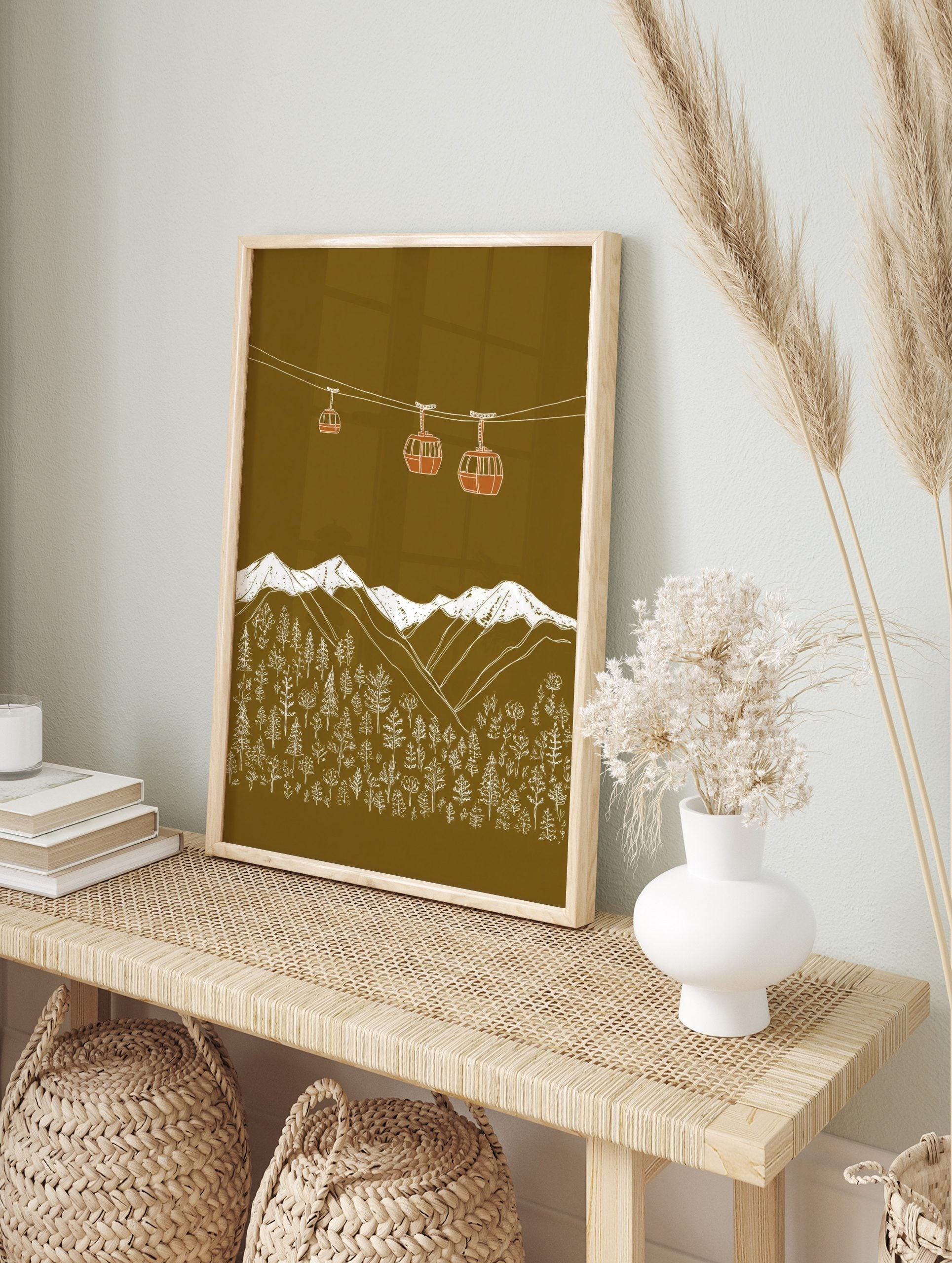 Illustrative gondola cabins above snow-capped mountains and forest on an olive green, in an alternate framed mockup