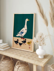 Illustrative print of a white goose with blue wings and four ducklings, three black and one, in an alternate framed mockup