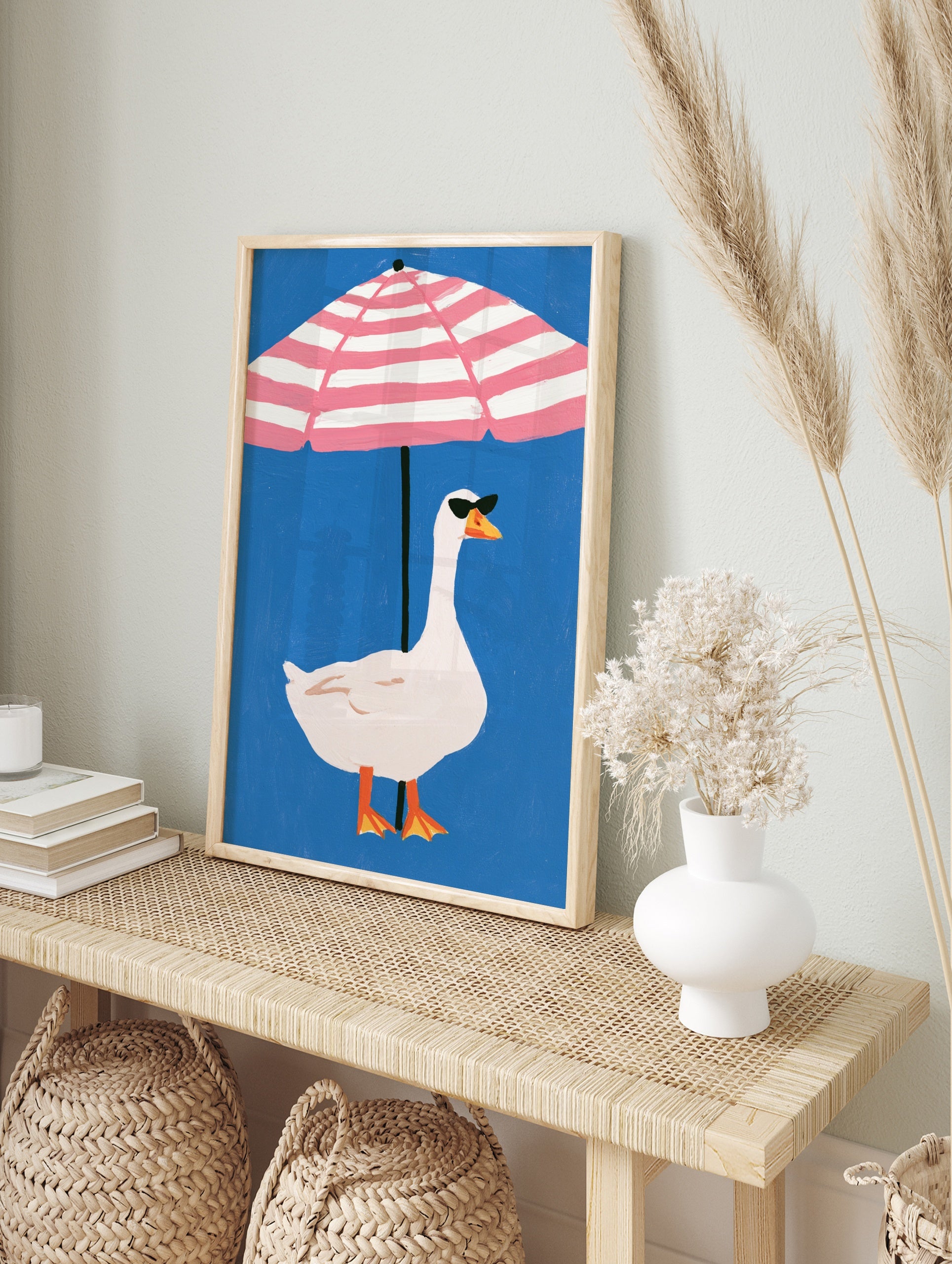 Playful illustration of a white goose in sunglasses under a pink and white striped beach, in an alternate framed mockup
