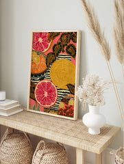 Illustrative art print of sliced red grapefruit, orange citrus, patterned leaves, and stripes, in an alternate framed mockup