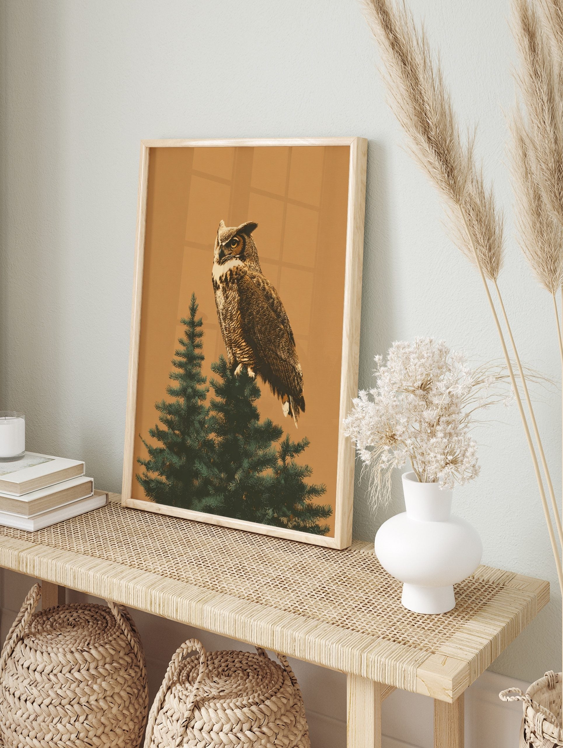 Illustrative great horned owl perched on a green evergreen tree branch against a warm tan, in an alternate framed mockup