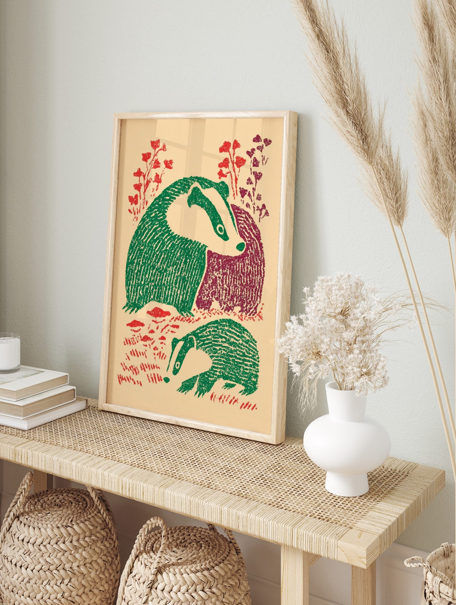 Illustrative print of two badgers with green and maroon bodies, red foliage, on a beige, in an alternate framed mockup